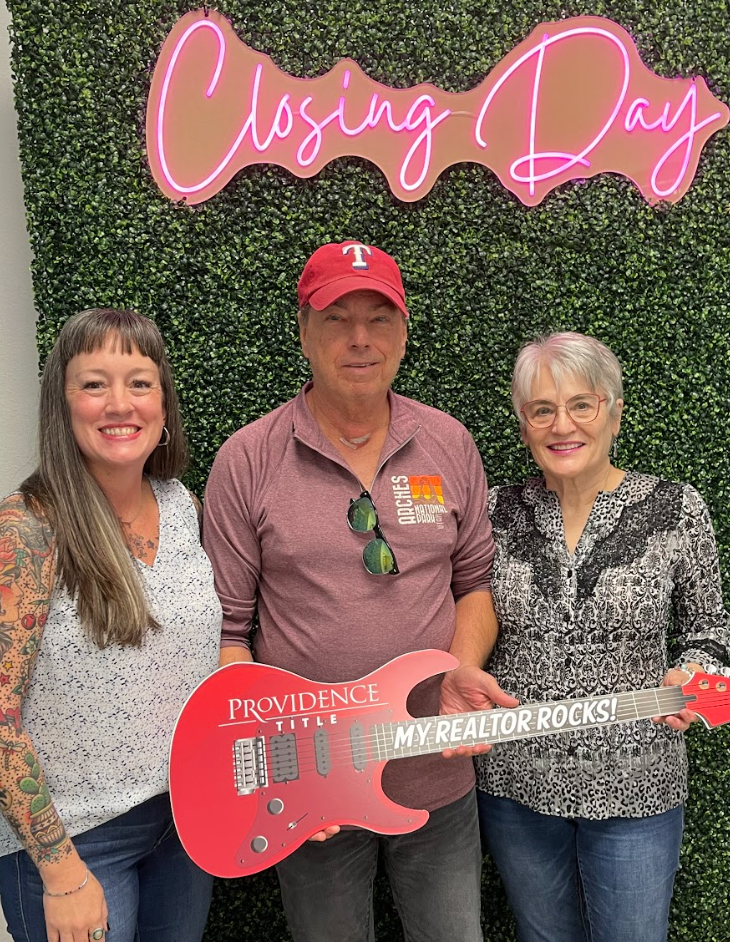 Smiling trio at closing day holding red guitar